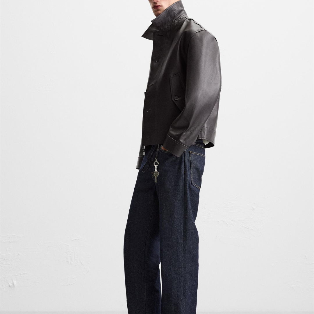 Men's black leather jacket with high collar, paired with dark denim jeans and keychain accessory
