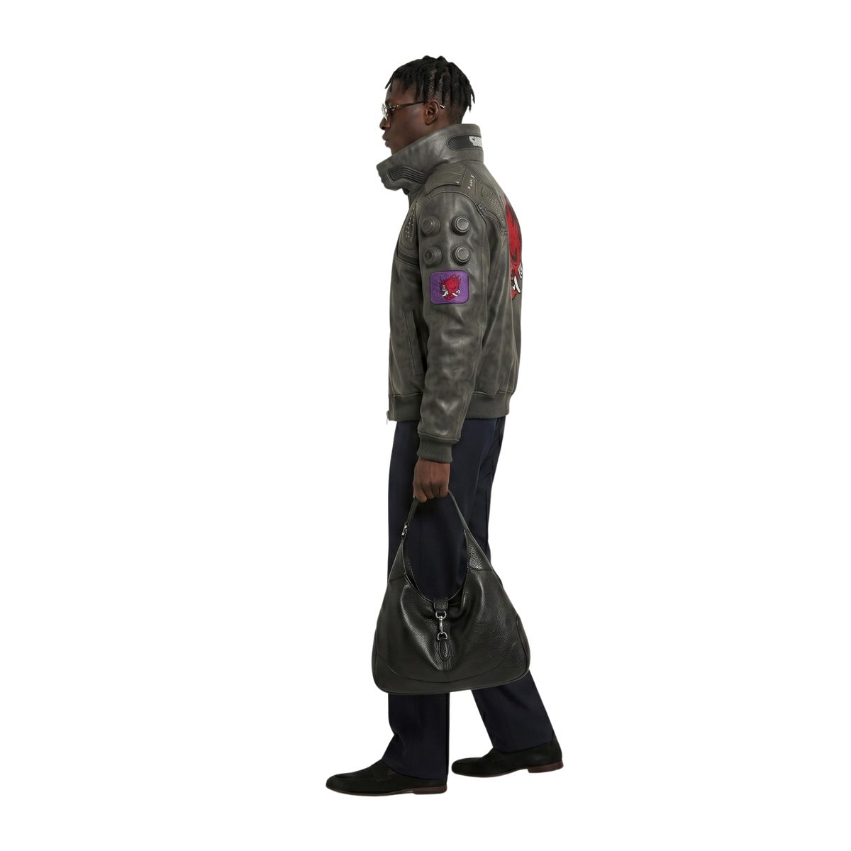 Man wearing olive green leather bomber jacket with red graphic patch, carrying black leather shoulder bag