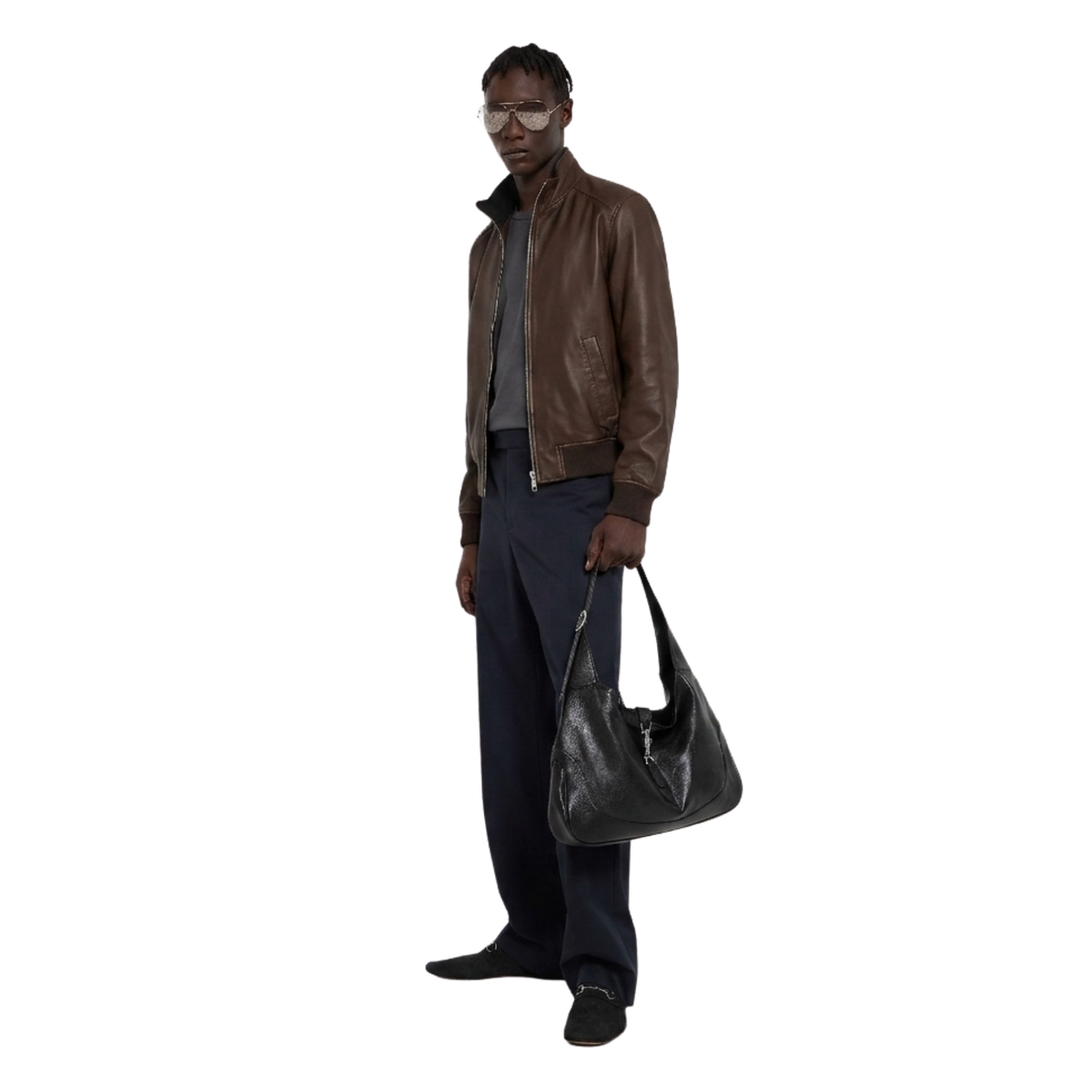 Man wearing brown leather bomber jacket, dark trousers, holding black shoulder bag, stylish casual outfit