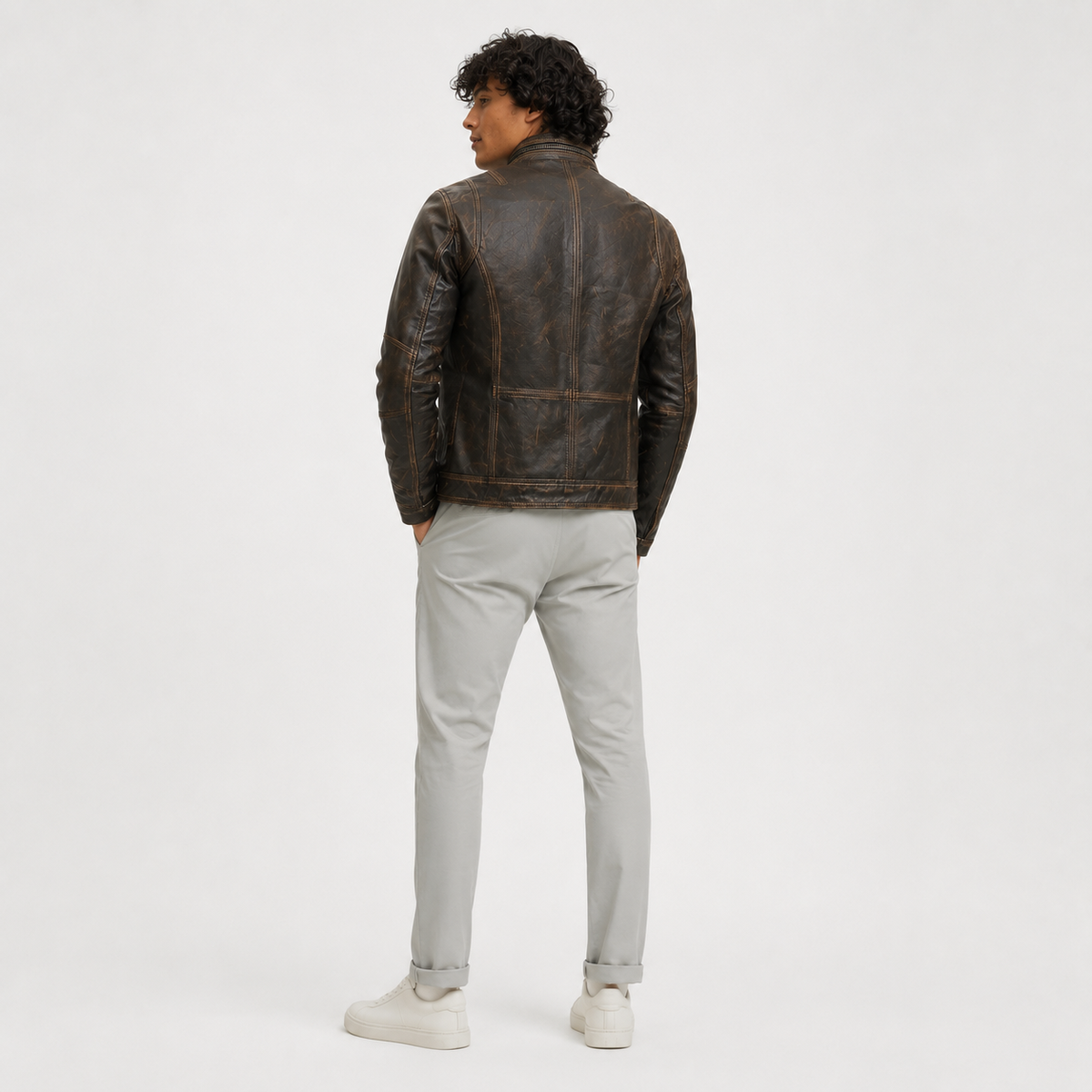 Men's distressed brown leather jacket with quilted back, paired with light gray pants and white sneakers