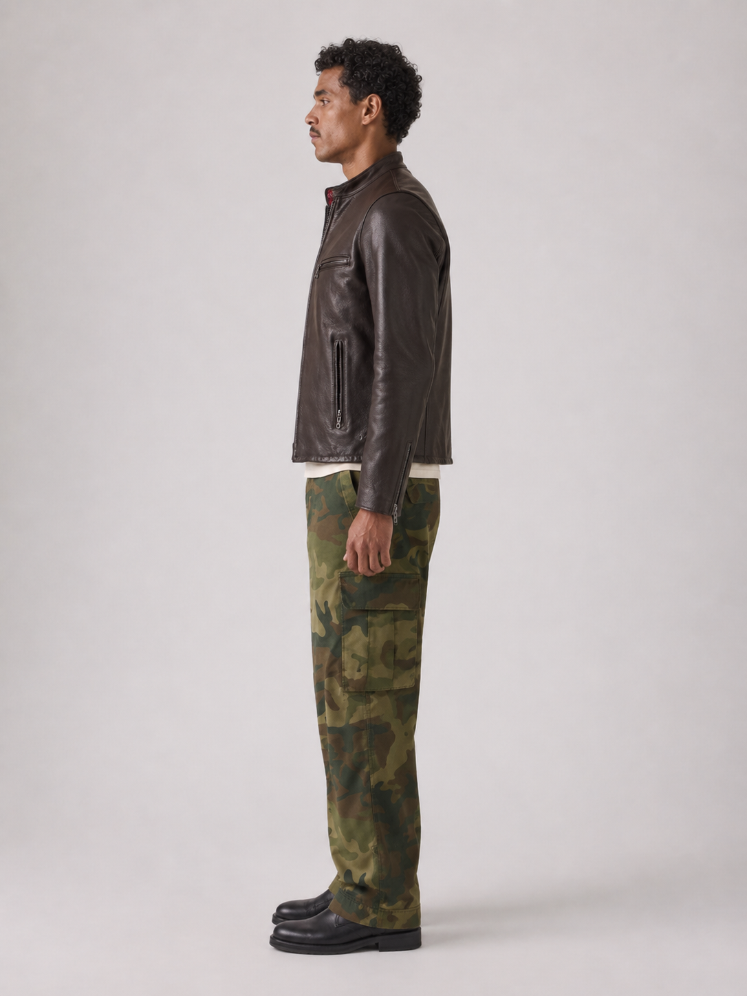 Man in brown leather jacket and green camouflage cargo pants, side profile studio shot