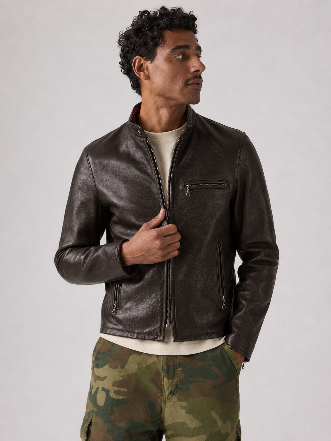 Man wearing dark brown leather jacket with zipper pockets, styled with camo pants and cream tee