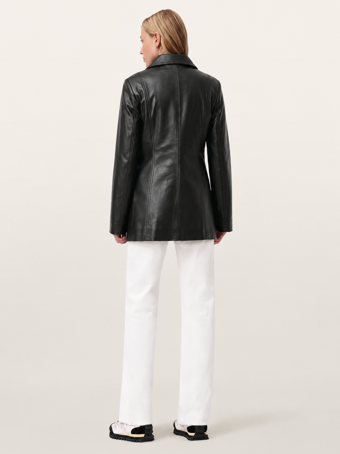 Black leather jacket with structured back, worn with white pants and chunky sneakers