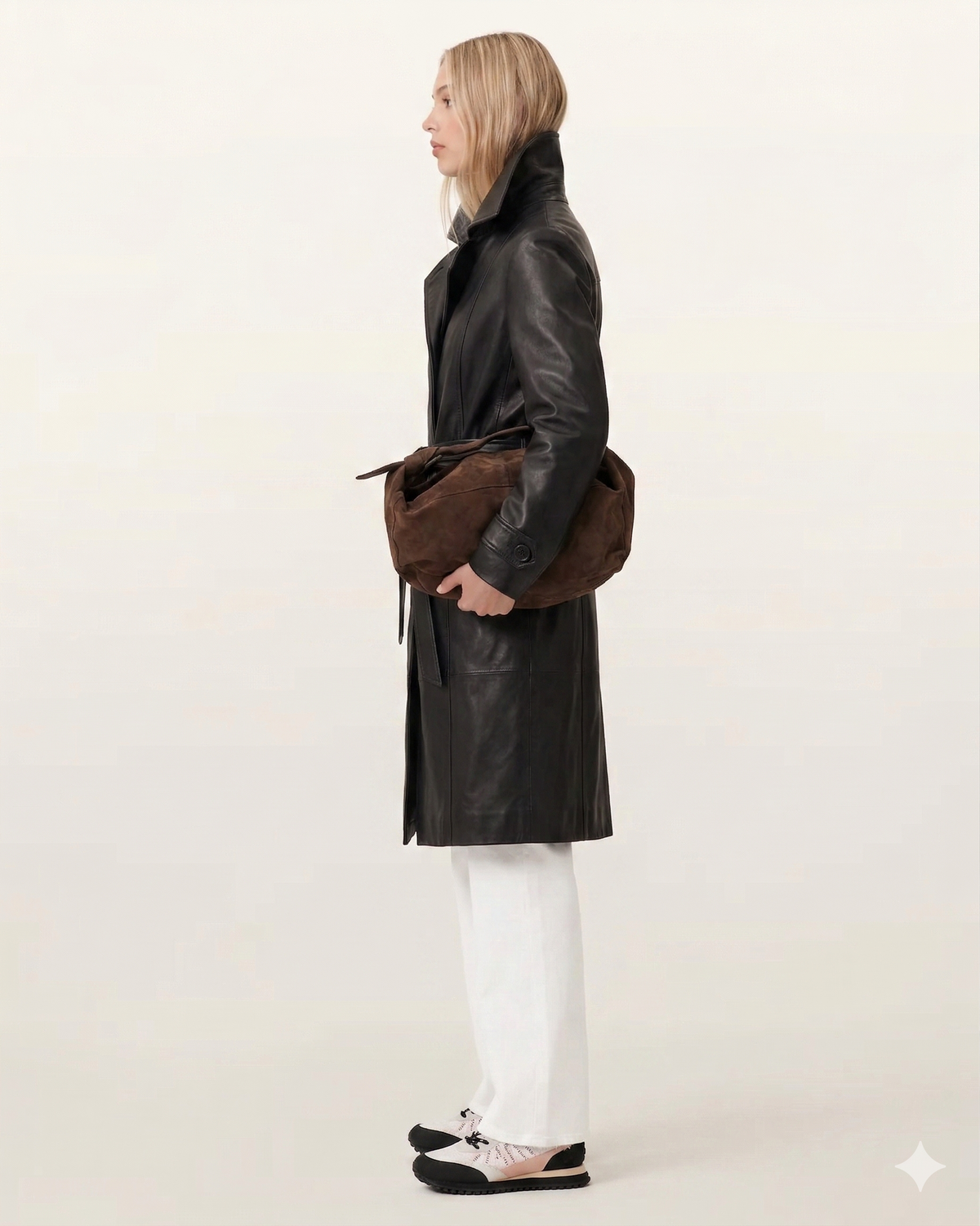 Woman in black leather coat with brown suede bag, white pants, and sneakers