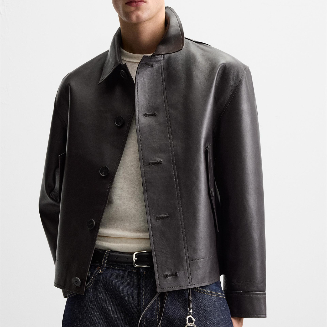 Men's black leather jacket with button front, worn over beige tee and dark jeans, modern casual style