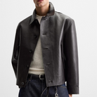 Men's black leather jacket with button front, worn over beige tee and dark jeans, modern casual style
