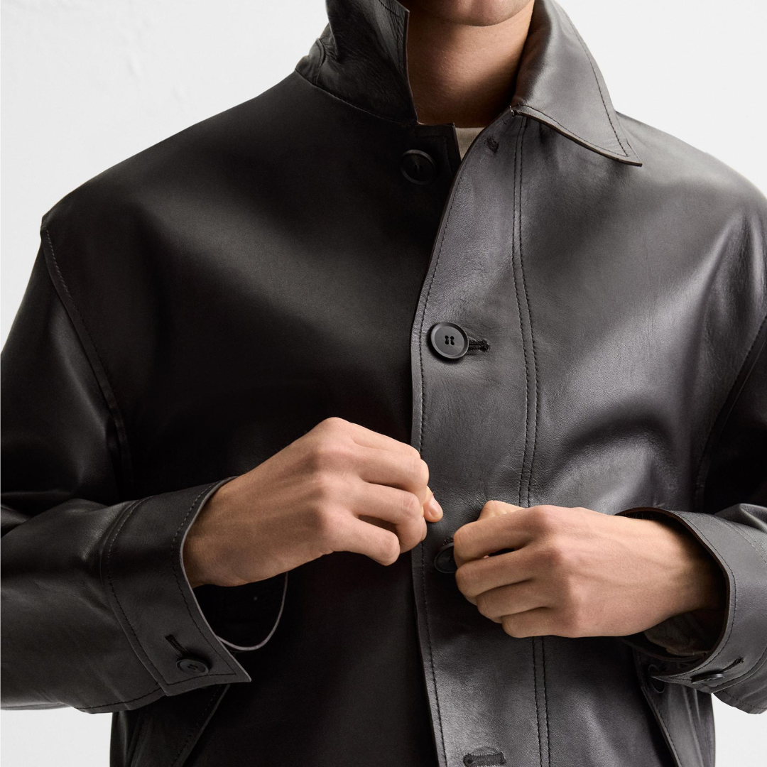 Man buttoning a sleek black leather jacket with classic collar and cuffs