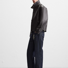 Men's black leather jacket with high collar, paired with dark denim jeans and keychain accessory