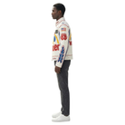 Man wearing white racing jacket with flame graphics, American flag, and sponsor logos, paired with dark jeans and white sneakers