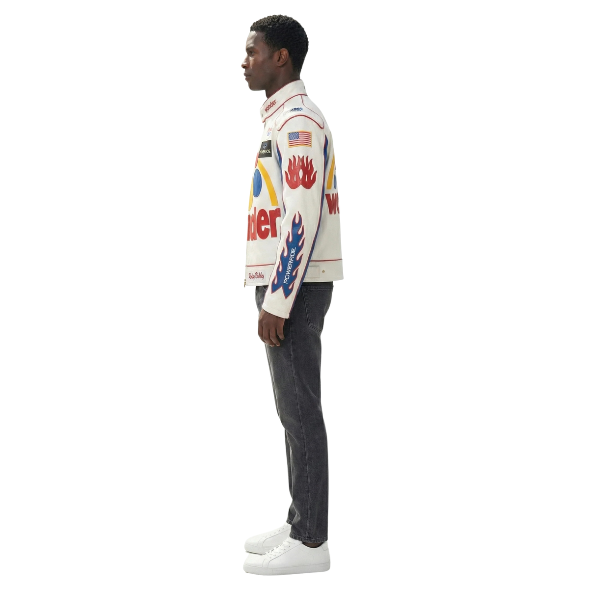 Man wearing white racing jacket with flame graphics, American flag, and sponsor logos, paired with dark jeans and white sneakers