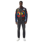 Man wearing black and blue racing-style leather jacket with colorful logos and 'Wonder' text, paired with dark jeans and white sneakers