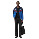 Men's blue and navy track jacket with red stripes, worn with black jeans and tote bag