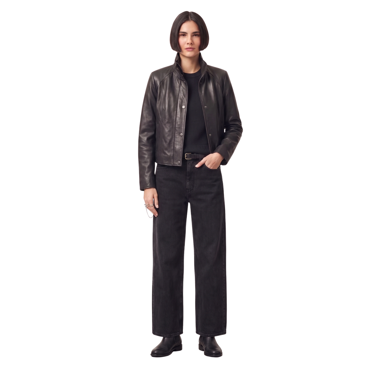 Woman in black leather jacket, ribbed sweater, wide-leg jeans, and boots, hands in pockets, studio shot