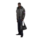 Man wearing stylish gray leather bomber jacket with hood, holding black shoulder bag, modern urban fashion