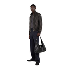 Man wearing black leather bomber jacket, navy pants, and holding a black leather bag