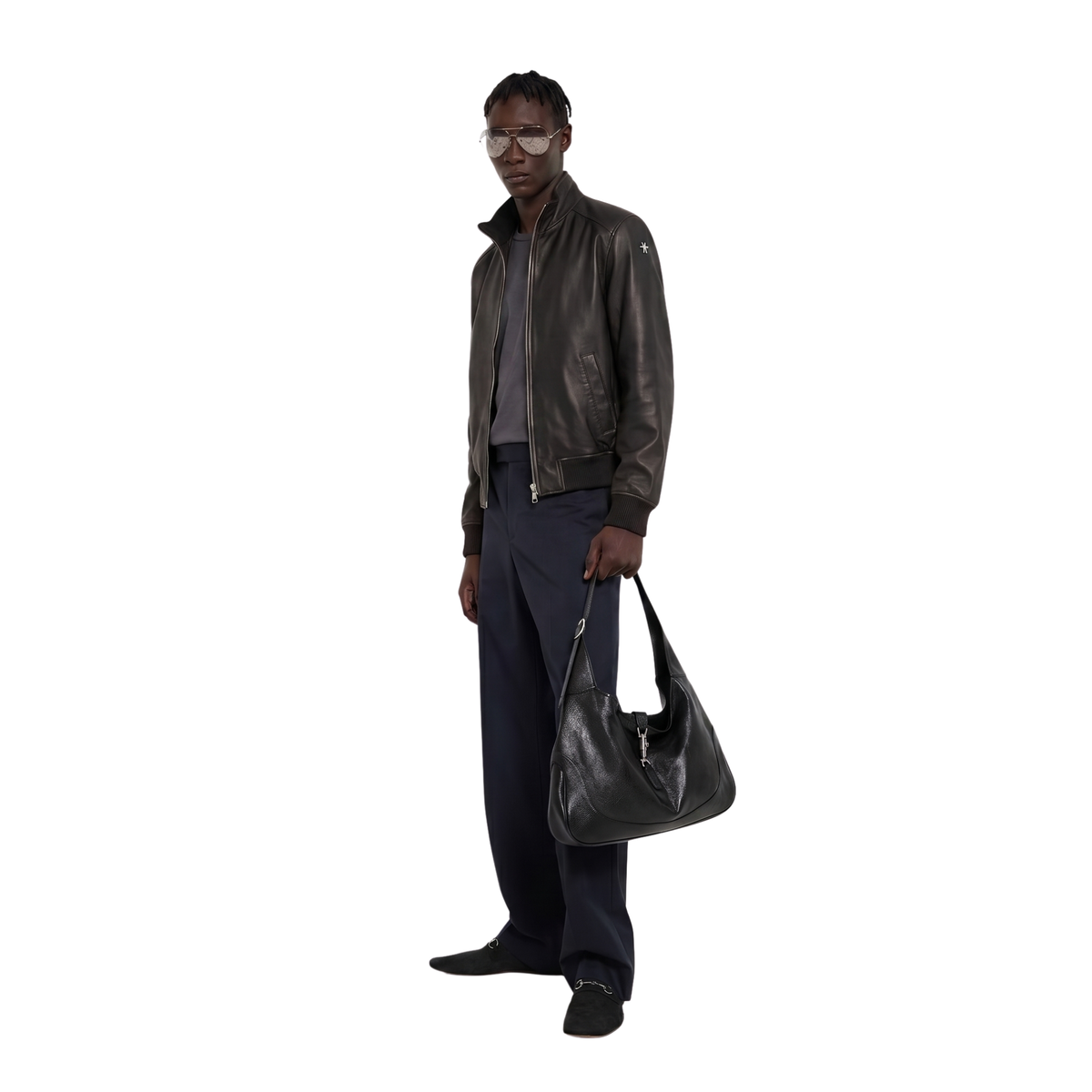 Man wearing black leather bomber jacket, navy pants, and holding a black leather bag