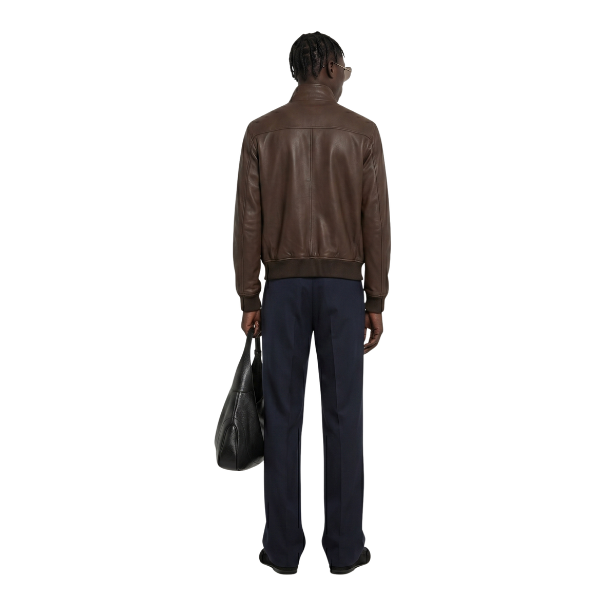 Man wearing brown leather bomber jacket, navy trousers, holding black leather bag, back view