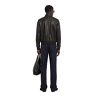 Man wearing black leather jacket and navy trousers, holding black bag, back view