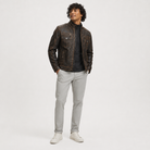Man wearing distressed brown leather jacket with quilted shoulders, paired with light gray pants and white sneakers