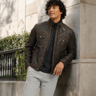 Man wearing distressed brown leather jacket with zip pockets, styled urban casual against stone wall