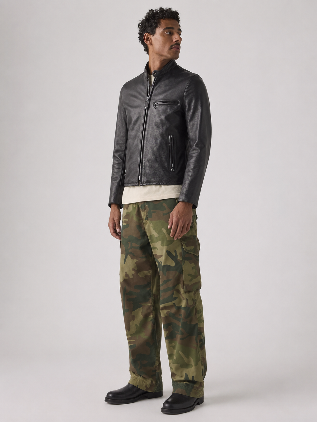 Men's black leather moto jacket with zipper pockets, paired with green camouflage cargo pants and black boots