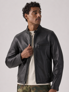 Men's black leather jacket with zippered pockets and stand collar, styled with camo pants
