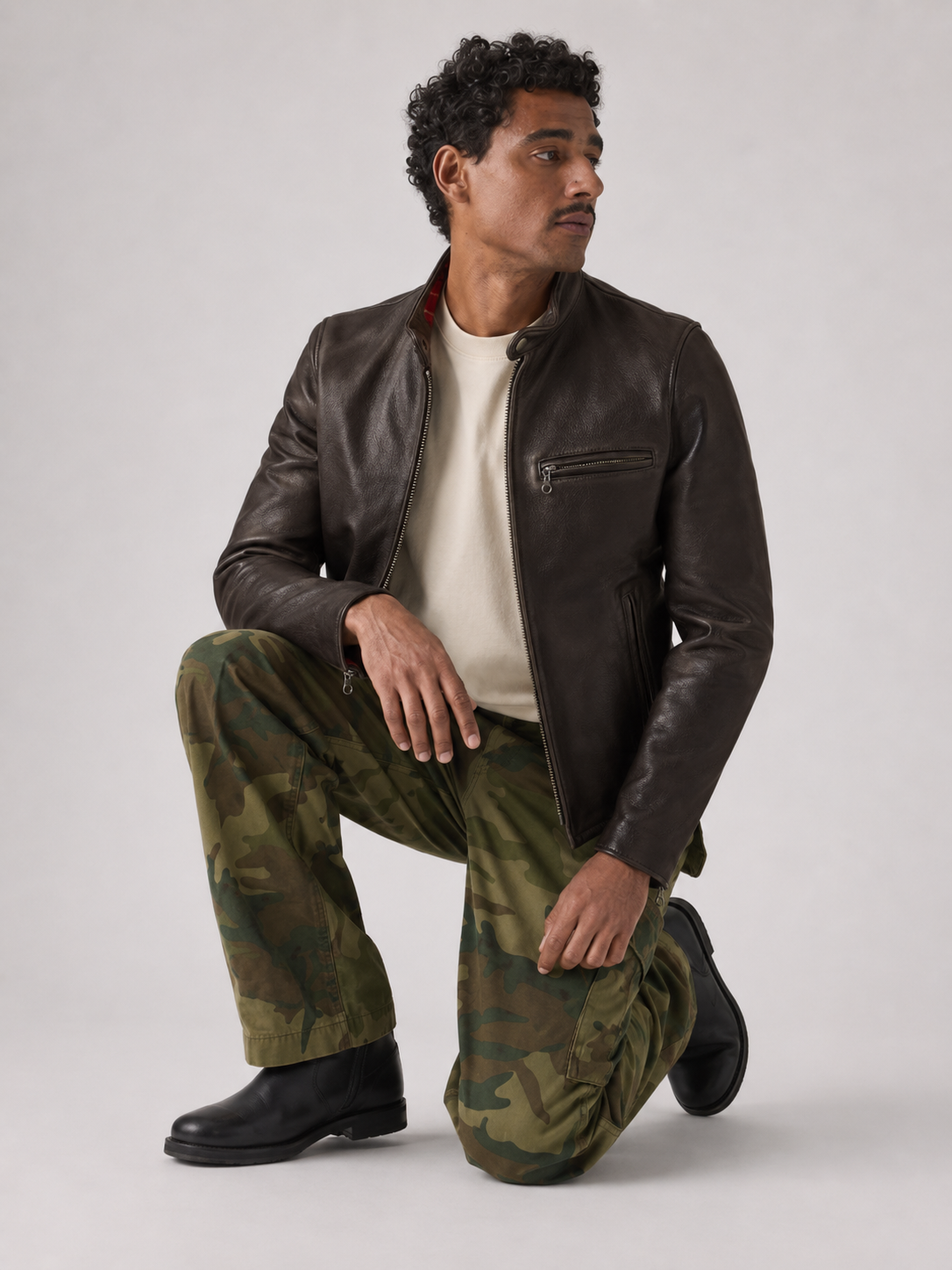 Man in brown leather jacket, camo pants, black boots, crouching pose