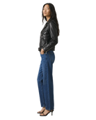 Woman in black leather moto jacket and wide-leg blue jeans, side view