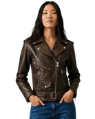 Woman wearing brown distressed leather moto jacket with zippers and belt, paired with blue jeans