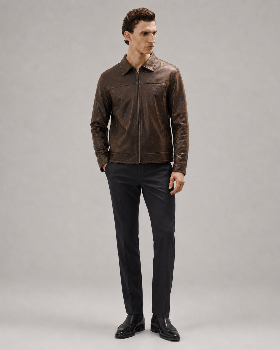 Man wearing brown leather jacket with zipper, black trousers, and dress shoes on gray background