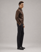 Man in brown leather jacket with black trousers and dress shoes, side profile