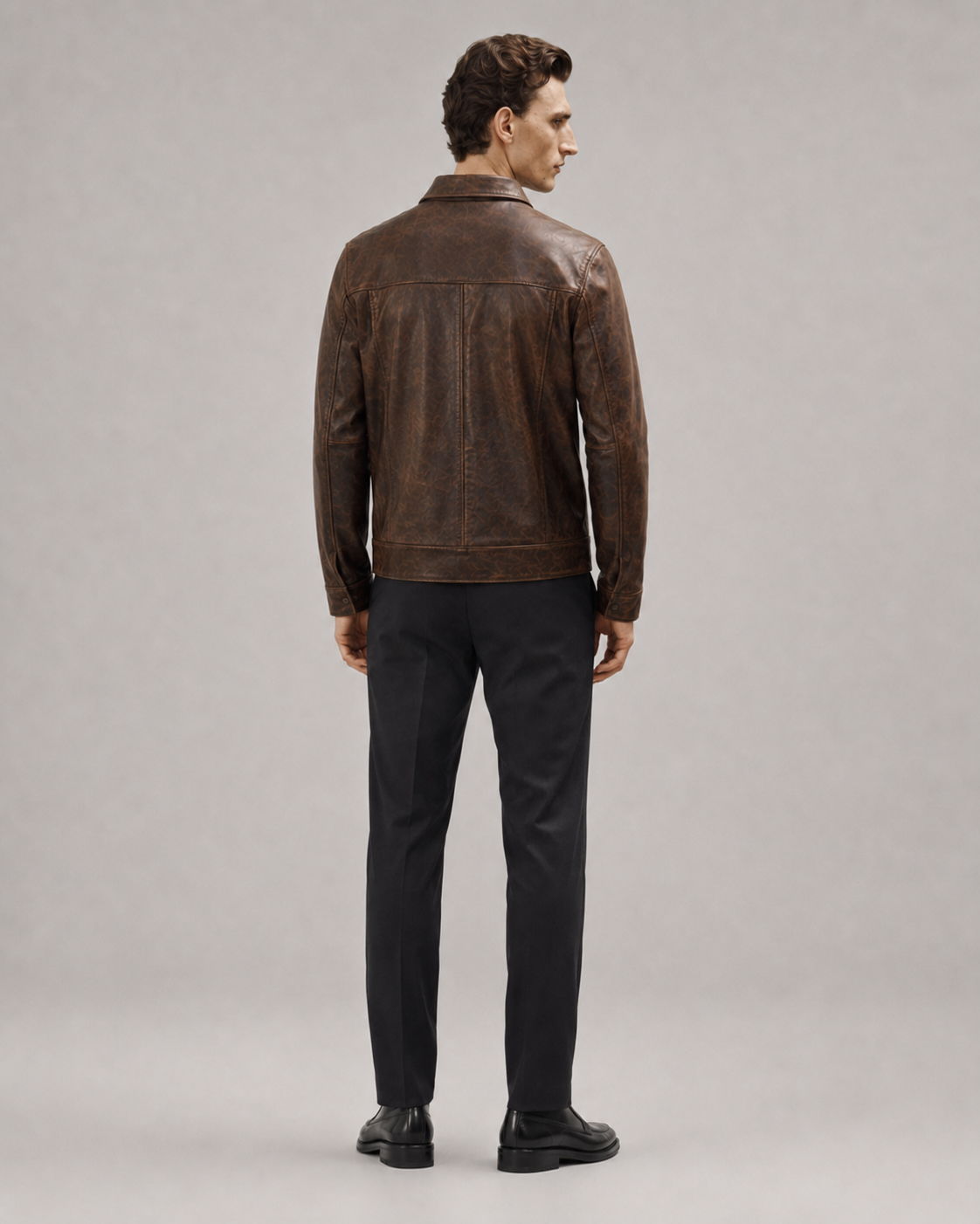 Man wearing brown leather jacket with vintage texture, black trousers, and dress shoes, back view