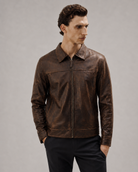 Men's brown distressed leather jacket with zip front and collar, styled with black pants