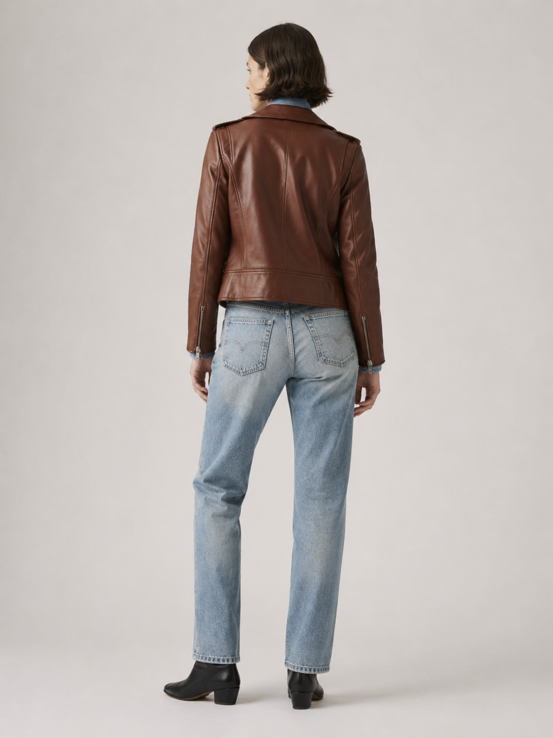 Brown leather jacket with blue jeans and black boots, back view