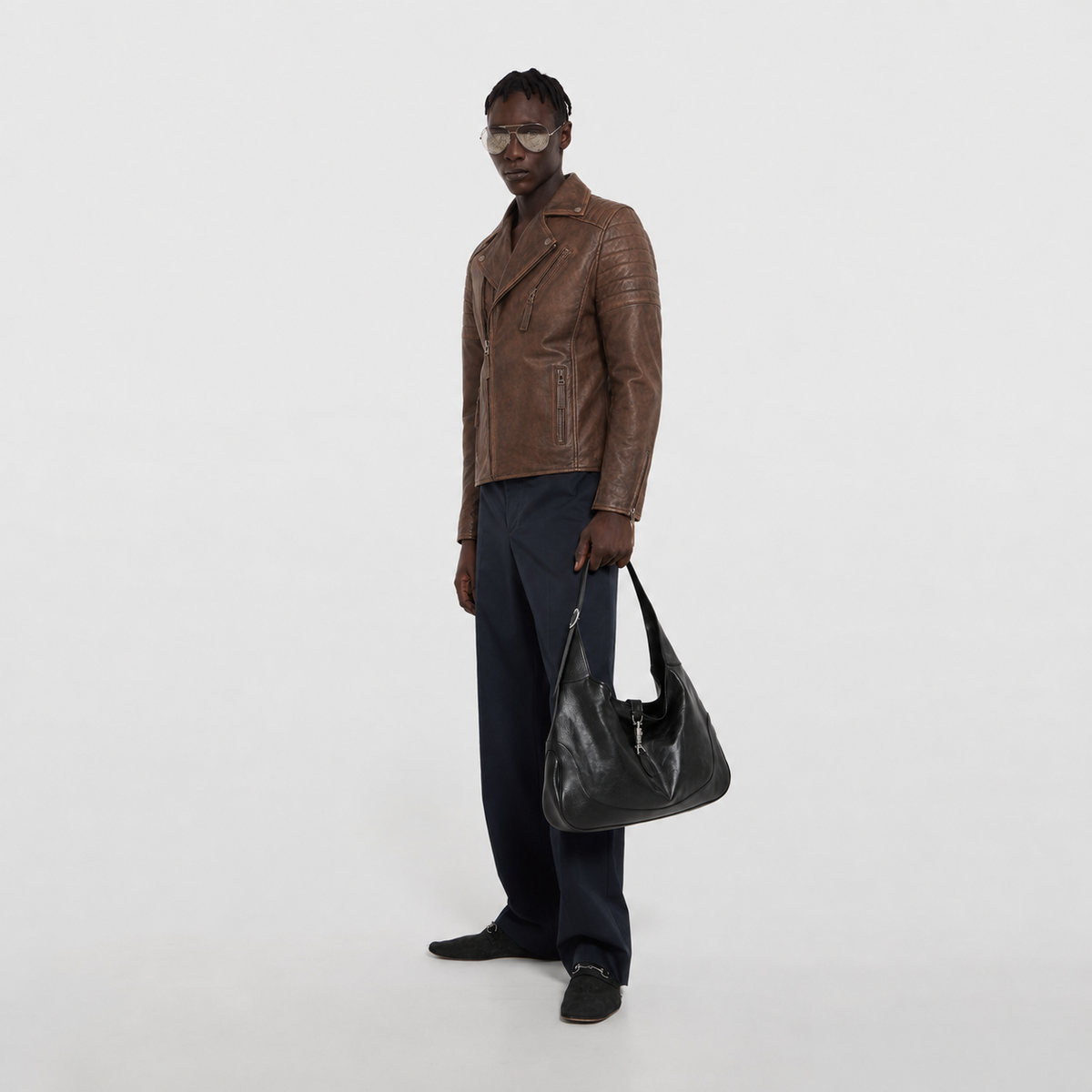 Man in brown leather jacket holding black shoulder bag, stylish casual outfit