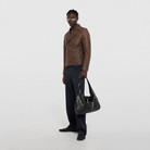 Man in brown leather jacket holding black shoulder bag, stylish casual outfit
