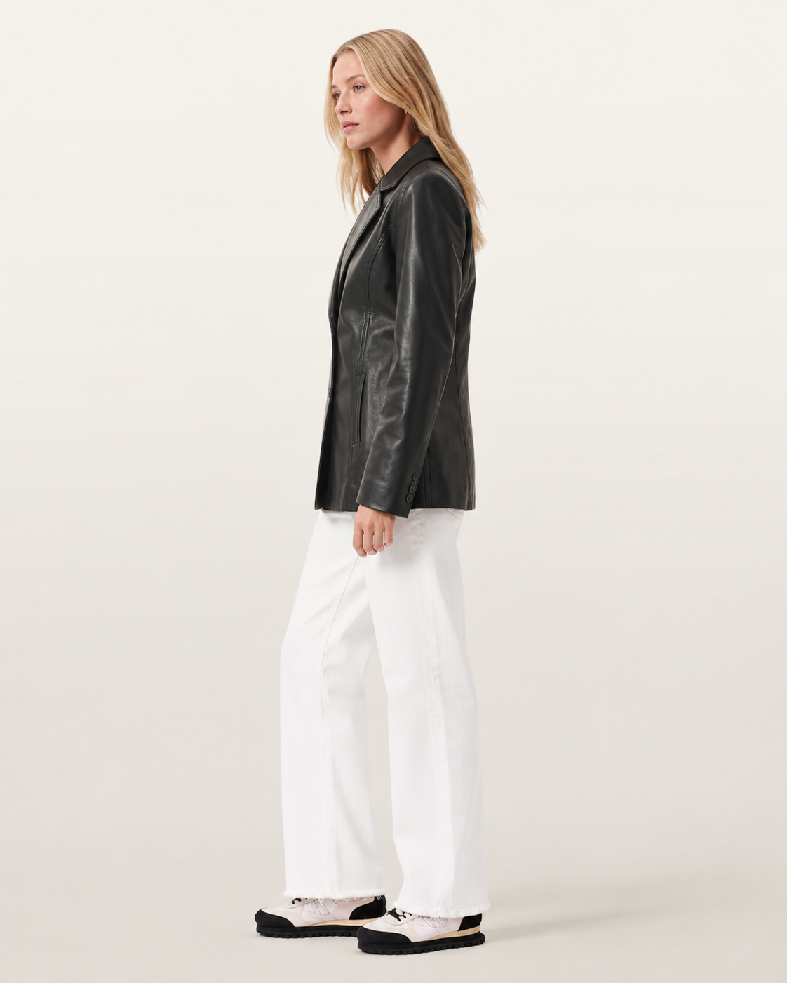 Woman in black leather jacket, white wide-leg jeans, and sneakers, side view