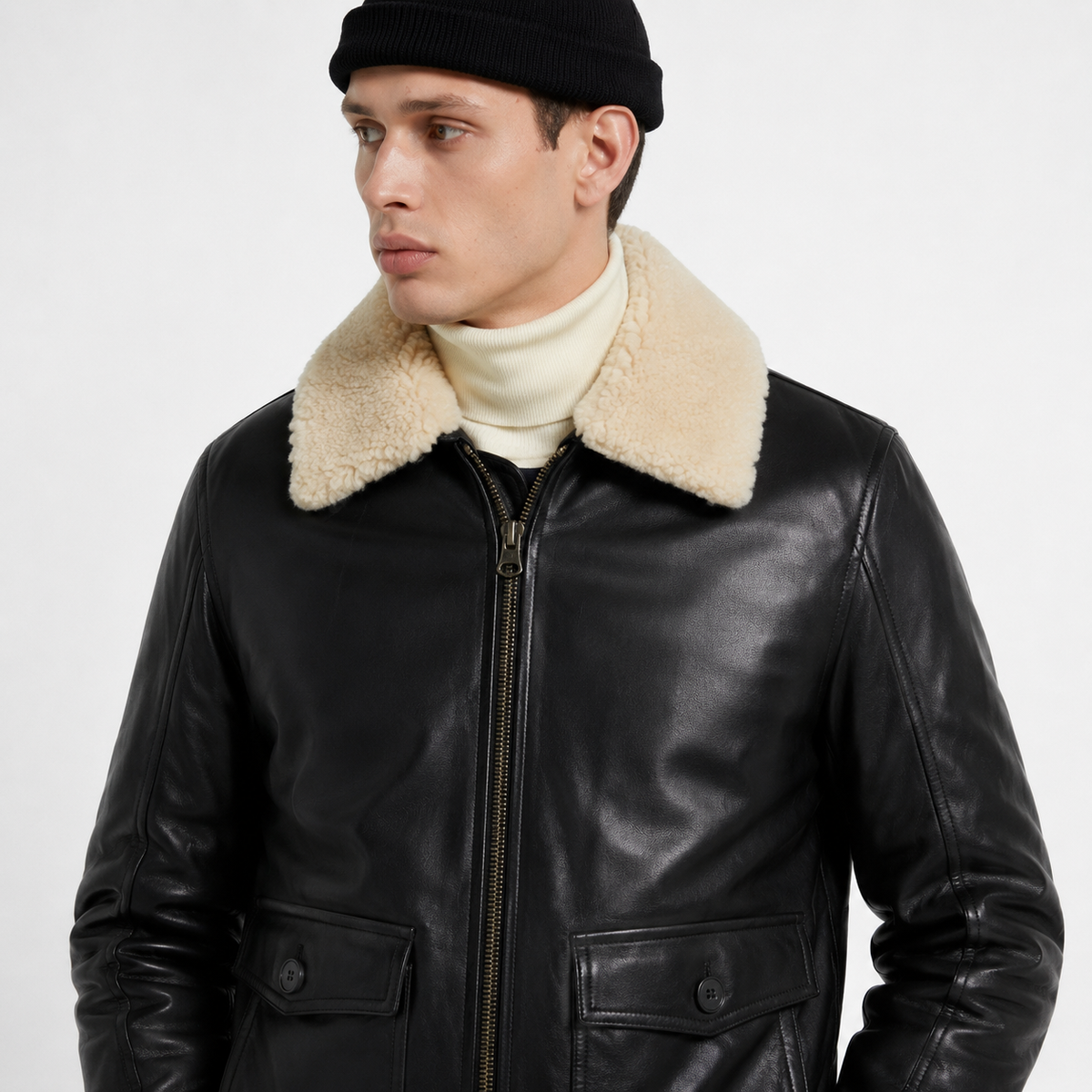 Men's black leather bomber jacket with shearling collar, worn over cream turtleneck, styled with black beanie