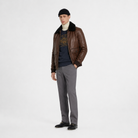 Men's brown leather bomber jacket with shearling collar, styled with gray trousers and black loafers