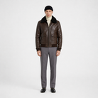 Men's brown leather bomber jacket with shearling collar, styled with turtleneck and gray trousers