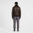Men's brown leather bomber jacket with shearling collar, back view, paired with gray trousers and black beanie