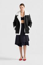 Black shearling aviator jacket with white fur trim, styled with navy pleated skirt and red heels