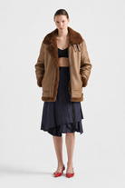 Brown shearling aviator jacket with fur collar, paired with navy pleated skirt and red heels