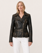 Women's distressed black leather moto jacket with belt and front pockets, paired with white jeans