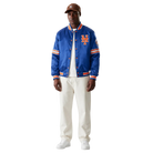 Men's royal blue Mets satin bomber jacket with orange trim and team logo, styled with white pants and cap