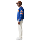 Man wearing blue New York Mets varsity jacket with orange trim, white pants, and brown cap