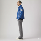 Man wearing blue leather jacket with patch, gray jeans, and black sneakers