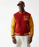 Red and gold varsity jacket with embroidered M letter, worn with baseball cap and white pants