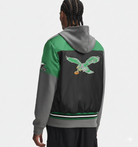 Green and gray varsity jacket with eagle embroidery, hooded design, and striped hem