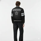 Black Cowboys varsity jacket with star logo, striped sleeves, and back text, worn by model in studio